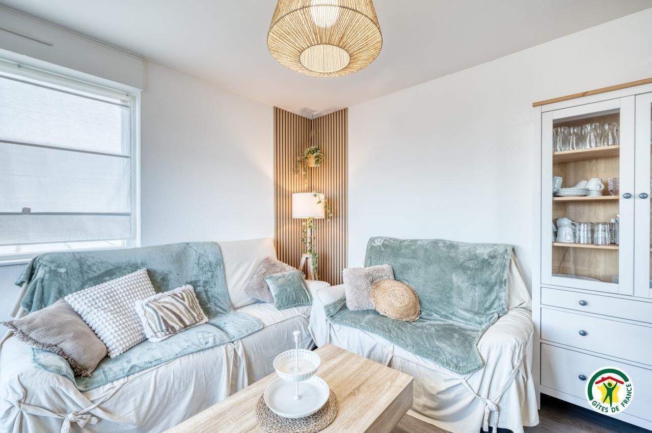 Un salon chaleureux avec deux canapés bleu clair, un meuble en bois contenant de la verrerie et un luminaire suspendu.
