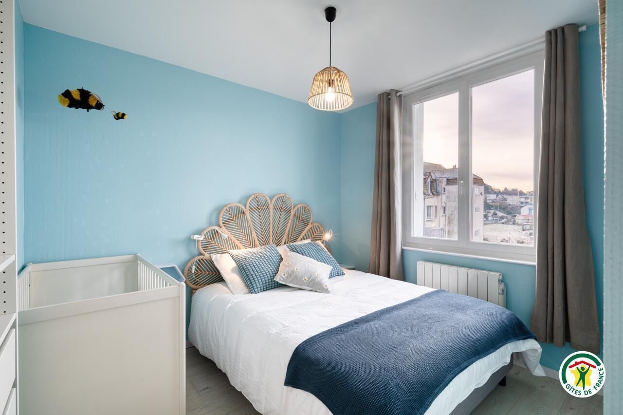 Une chambre à coucher avec un lit, un berceau, une fenêtre avec des rideaux et une vue sur la ville.