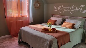 Une chambre à coucher avec un lit, une table de chevet sur laquelle se trouve un plateau avec des articles pour le petit-déjeuner, un élément décoratif mural et des rideaux légers.