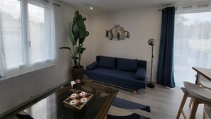 Un salon avec un canapé bleu, une table basse, une plante en pot et un luminaire fixé au mur.