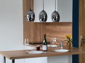 A modern kitchen with wooden cabinetry, a wooden countertop, three pendant lights, a wine bottle, and a vase with flowers.
