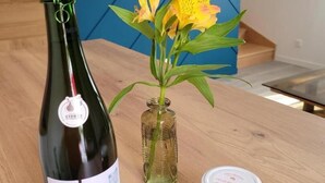 Une bouteille de vin, un pot de confiture et un vase rempli de fleurs, le tout posé sur une table en bois.