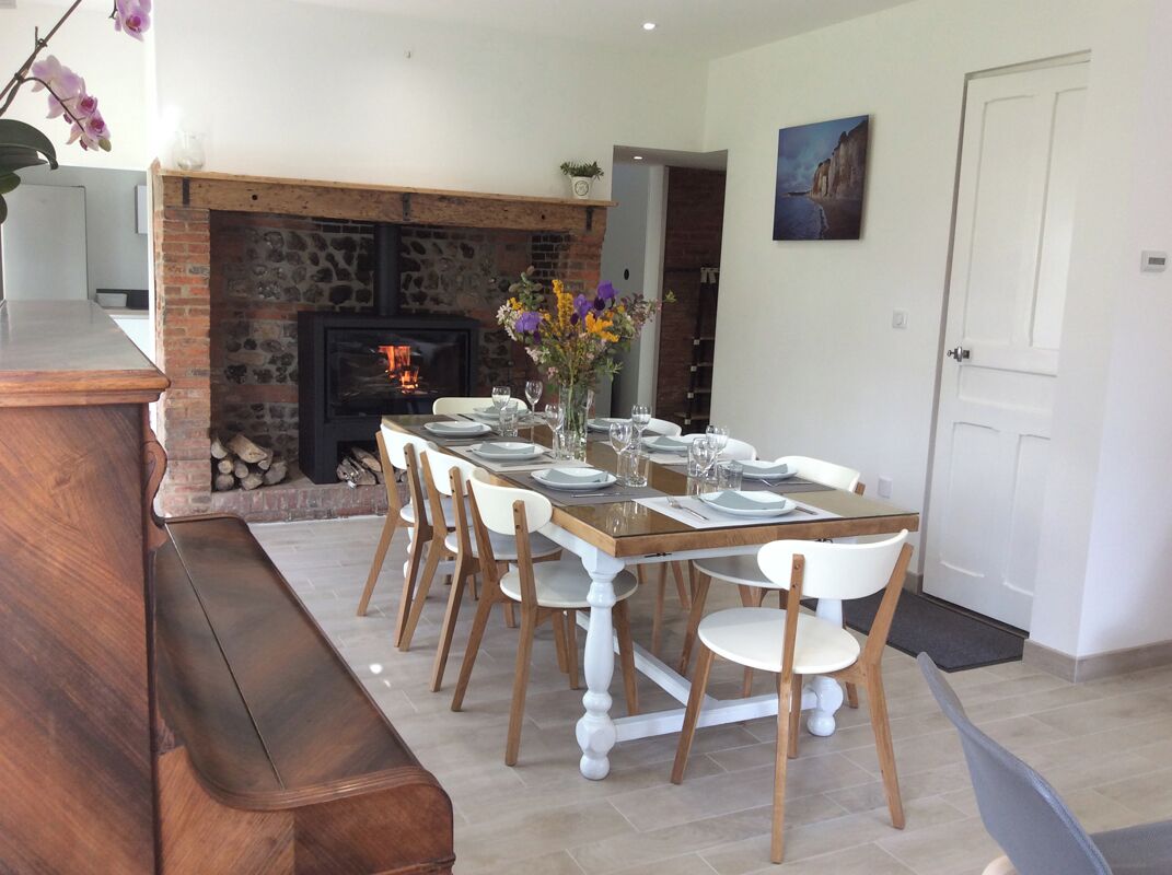 A dining area with a brick fireplace, white chairs, and a wooden table set for six.