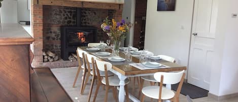 A dining area with a brick fireplace, white chairs, and a wooden table set for six.