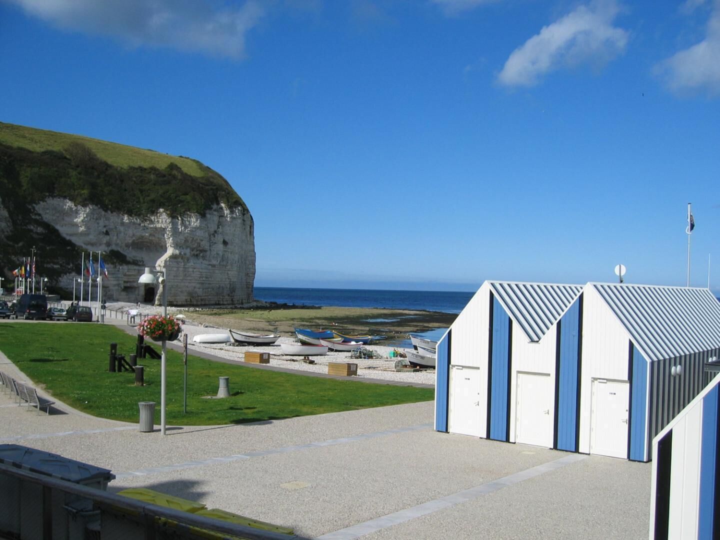 Un bâtiment situé sur la côte, doté d’un toit plat, d’une zone herbeuse où se trouvent des bateaux, et d’une falaise en arrière-plan.