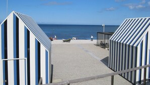 A beachside view with a clear sky, a sandy beach, and a row of striped beach huts.