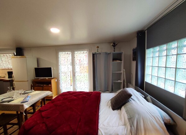 A bedroom with a bed, a table with a red blanket, a TV, and a window with a view.