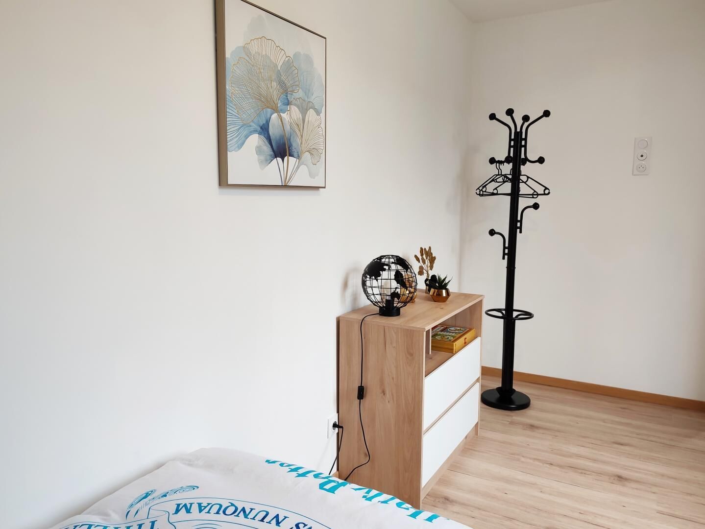 A room with a bed, a wooden nightstand, a globe, a plant, and a black floor lamp.