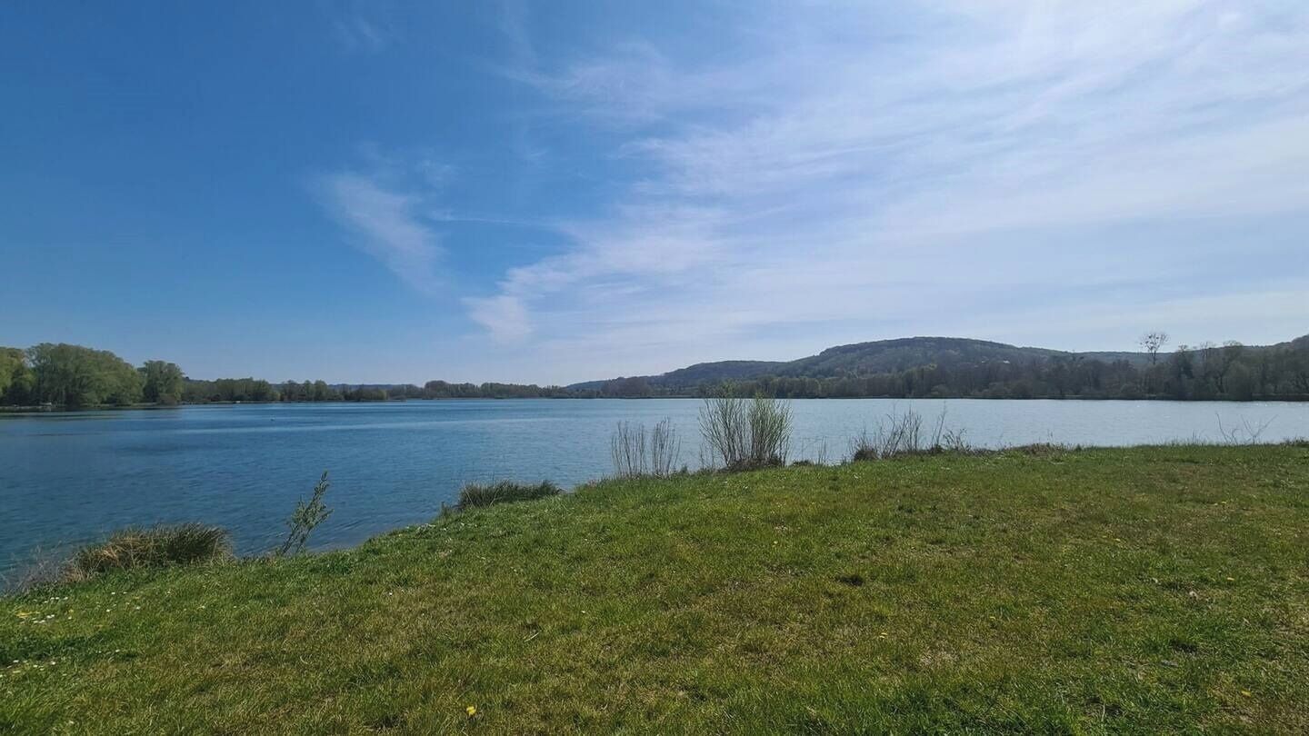 Un lago con rive erbose e colline lontane sotto un cielo sereno.