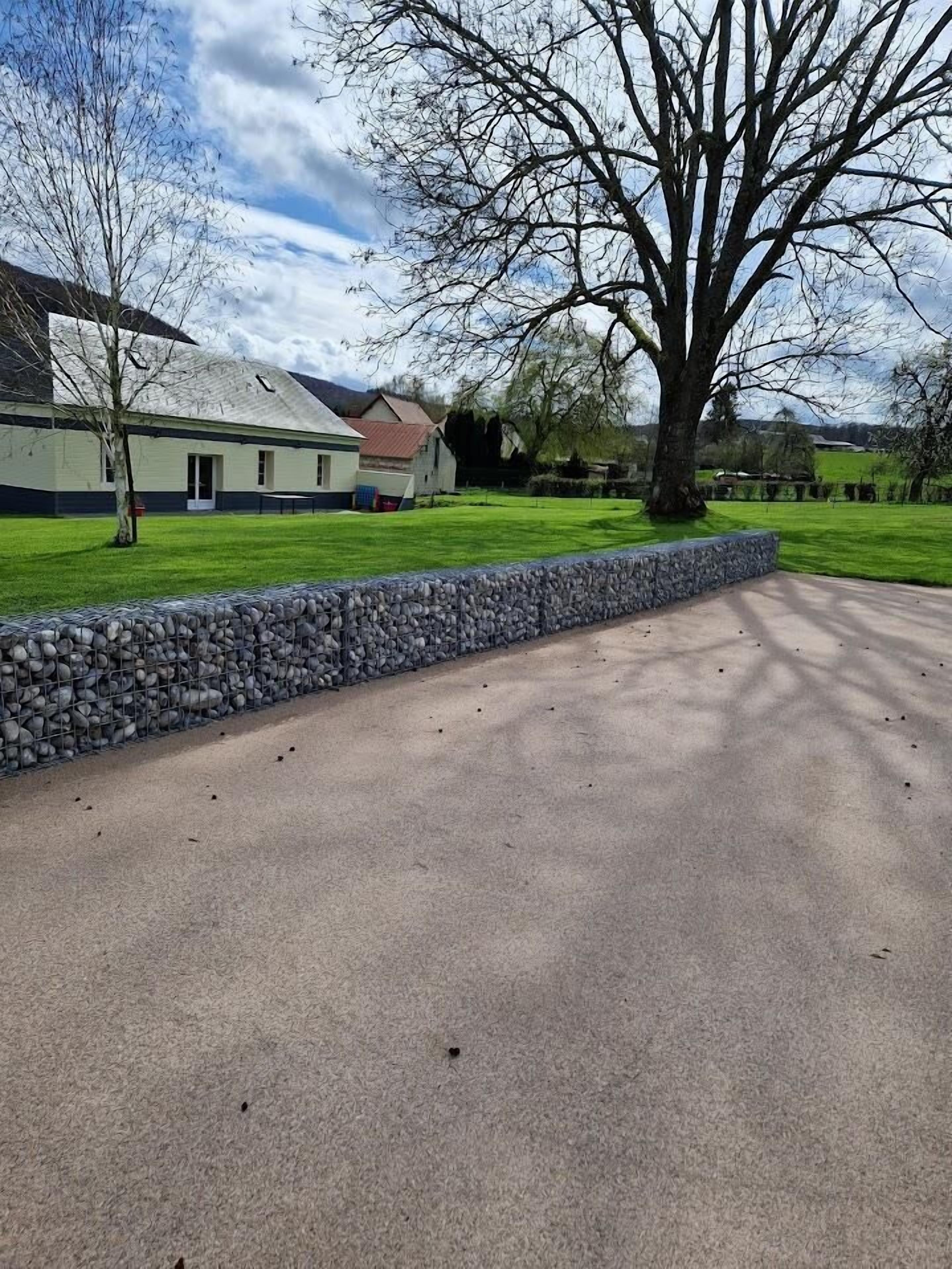 A paved driveway leading to a building with a stone wall and a grassy area.