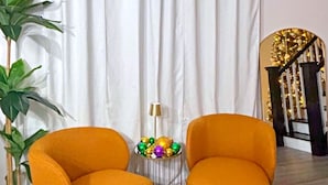 A room with two orange armchairs, a potted plant, a small table with decorative items, and a white curtain. - A Taste Of NOLA (LaPlace)