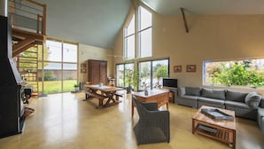 Un amplio salón con techo alto, una escalera de madera, un gran comedor, un sofá y una televisión.