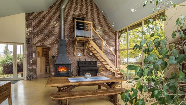 Un interior rústico con chimenea de ladrillo, escalera de madera y una mesa de comedor.