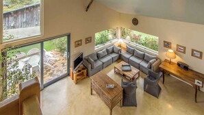 Amplia sala de estar con un sofá modular grande, una mesa de centro de madera y una televisión. Varias ventanas ofrecen luz natural y vistas al exterior.