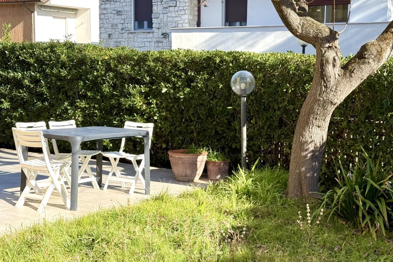 An outdoor seating area with a table and chairs, surrounded by greenery and a hedge.
