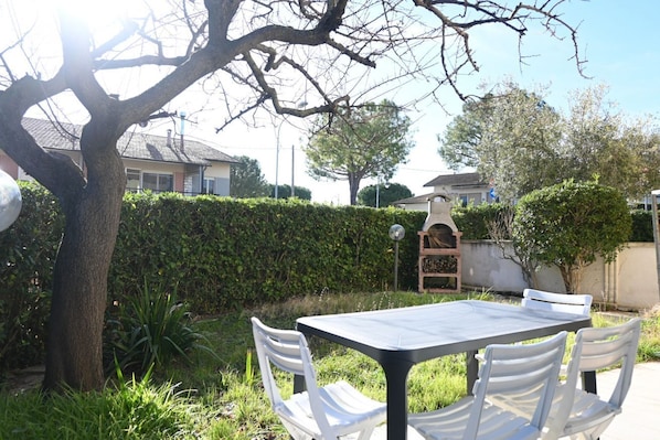 A patio with a table and chairs, surrounded by greenery and a tree.