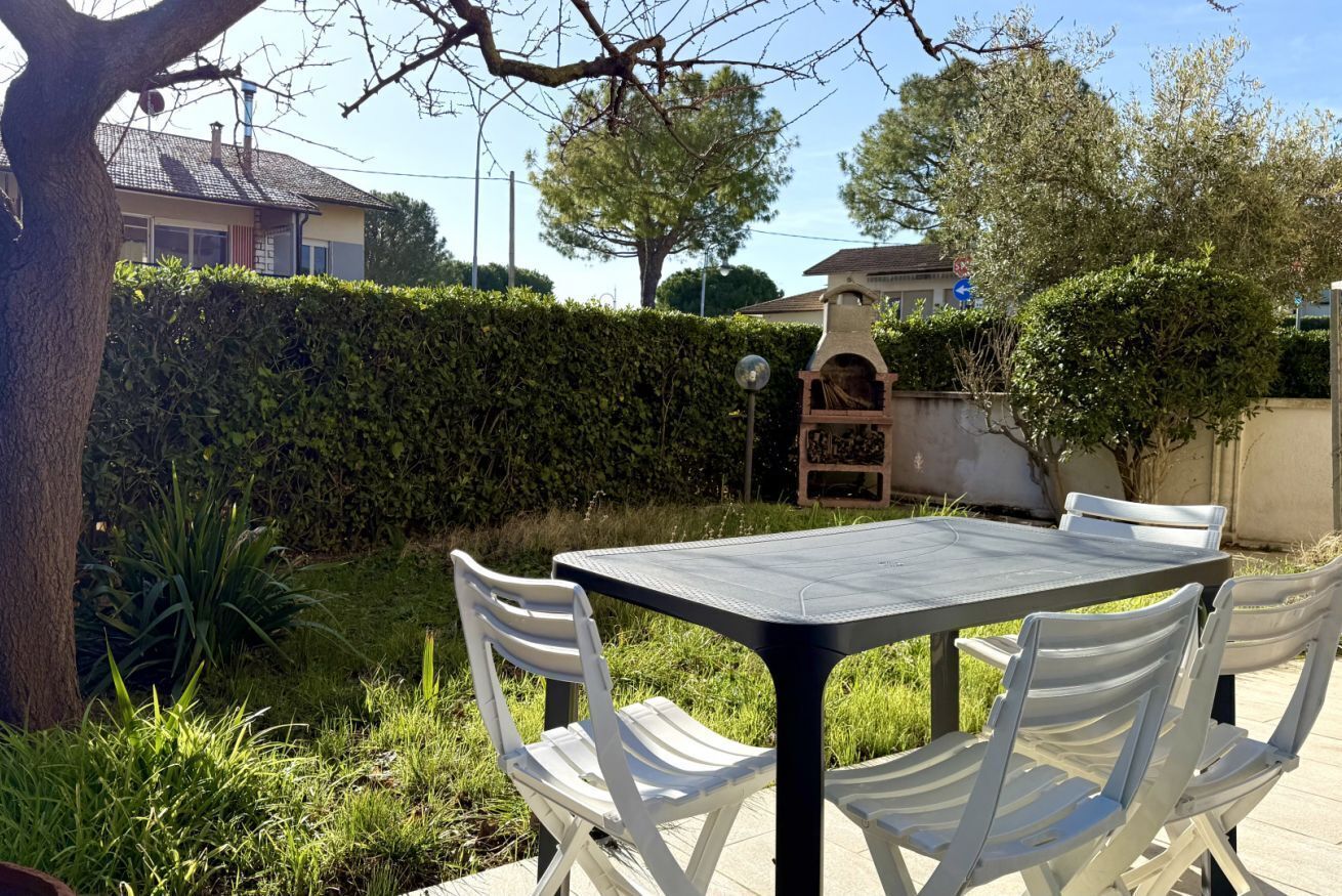 A patio with a table and chairs, surrounded by a hedge and trees.