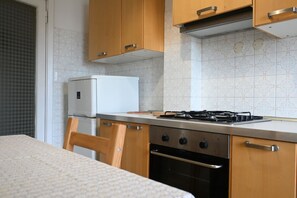 Une cuisine de taille réduite, dotée de meubles en bois, d’un réfrigérateur blanc, d’une cuisinière à gaz et d’un four.