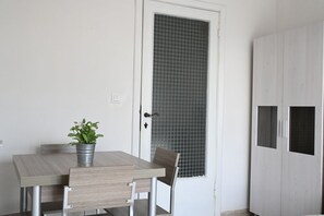 Une pièce comprenant une table en bois, une chaise, une plante en pot, une porte avec un panneau de verre texturé et une armoire.