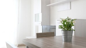 A modern dining area with a wooden table, metal bucket planter with flowers, and white cabinetry. - SE141 – Comfortable two-room apartment facing the sea (Senigallia)