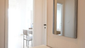 A bathroom with a white sink, a mirror, and a door leading to a room with a chair and a table. - SE141 – Comfortable two-room apartment facing the sea (Senigallia)