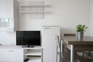 Une cuisine moderne équipée d’un téléviseur à écran plat, de meubles blancs et d’une table à manger avec des chaises.