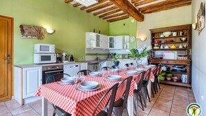 Un comedor con mantel a cuadros rojo y blanco, vigas de madera en el techo y una cocina al fondo.