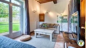 Un salón acogedor con techo de madera, un sofá, una mesa de centro y vistas a un jardín a través de amplios ventanales.