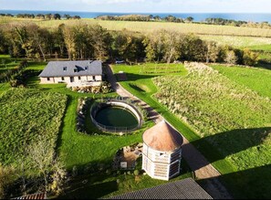 Ett flygbildsfoto av en fastighet med ett stort hus, en rund damm och en liten, tornliknande byggnad.