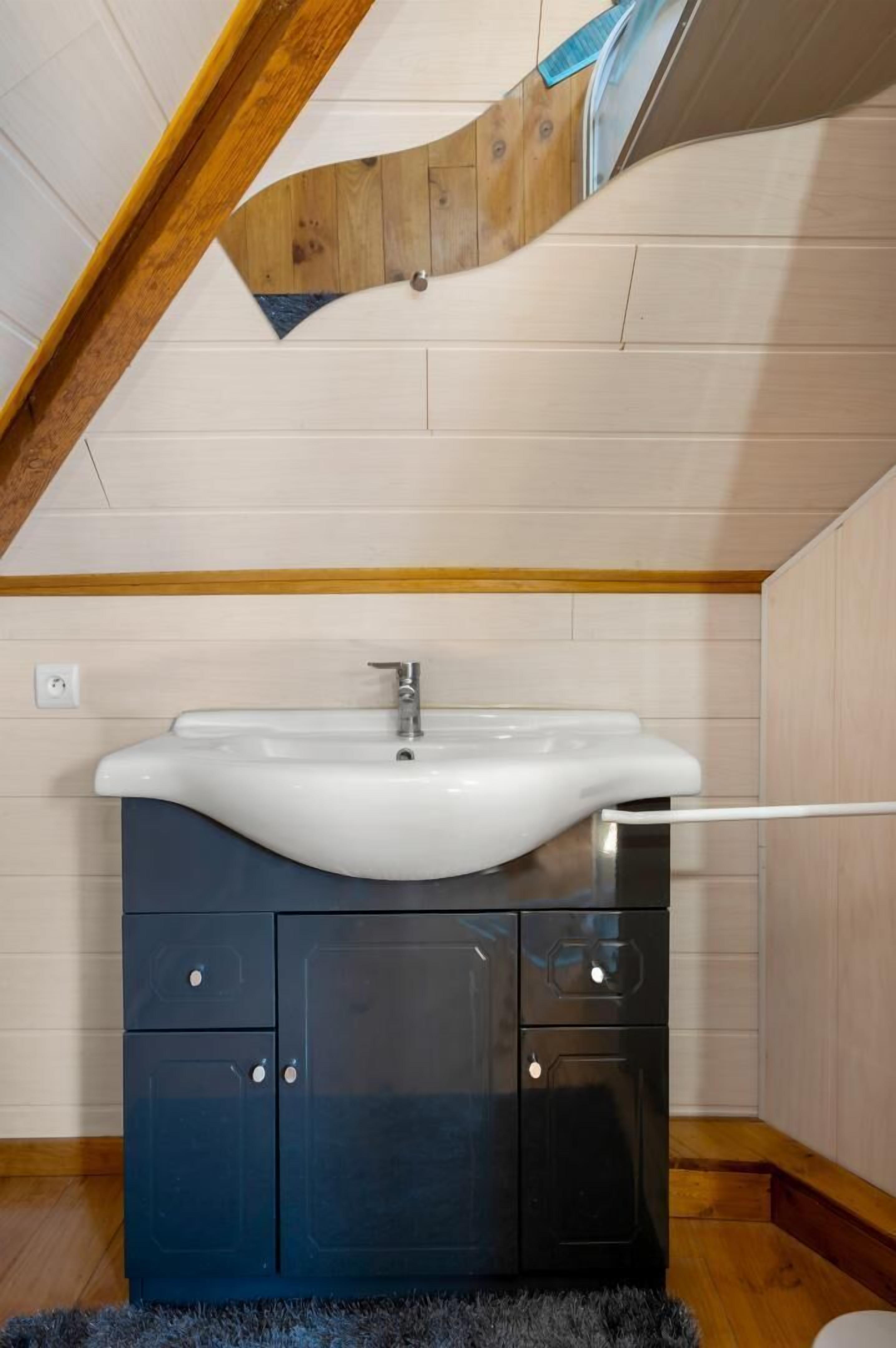 Une petite salle de bain avec un lavabo blanc, des meubles sombres et un plafond en bois.
