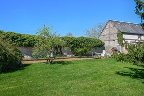 A grassy courtyard with a stone wall, a small wooden structure, and white outdoor furniture. - Gîtes de France® - The Duplex (DAMPIERRE EN BRAY)