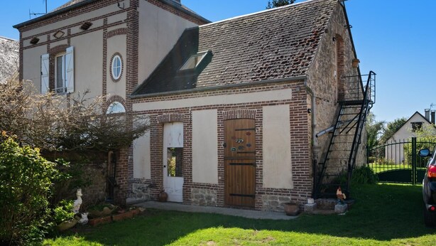 Un edificio de ladrillo tradicional con puerta de madera, un pequeño jardín y un coche estacionado afuera.