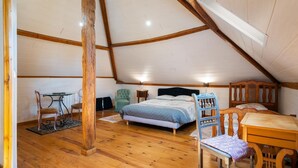 Habitación tipo tienda de campaña con techo alto y estructura de madera, que incluye una cama, dos sillas, una mesa y una lámpara de mesa pequeña.