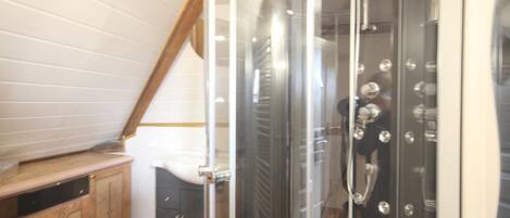 A shower with a glass enclosure, a wooden cabinet, and a sloped ceiling.