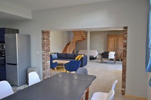 A modern kitchen with a refrigerator, a dining table with chairs, a sofa, and a staircase leading to an upper level.