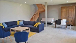 A modern living room with a sectional sofa, a wooden coffee table, and a dining area with chairs and a table.