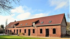 A brick building with a red-tiled roof, multiple windows, and a grassy lawn in front.