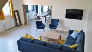 A living room with a sofa, chairs, a coffee table, and a dining area in the background.