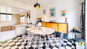 Une cuisine avec un carrelage à motifs, une table en marbre et un luminaire suspendu. Des tableaux encadrés ornent le mur, et une petite table y est posée, sur laquelle se trouve une plante.