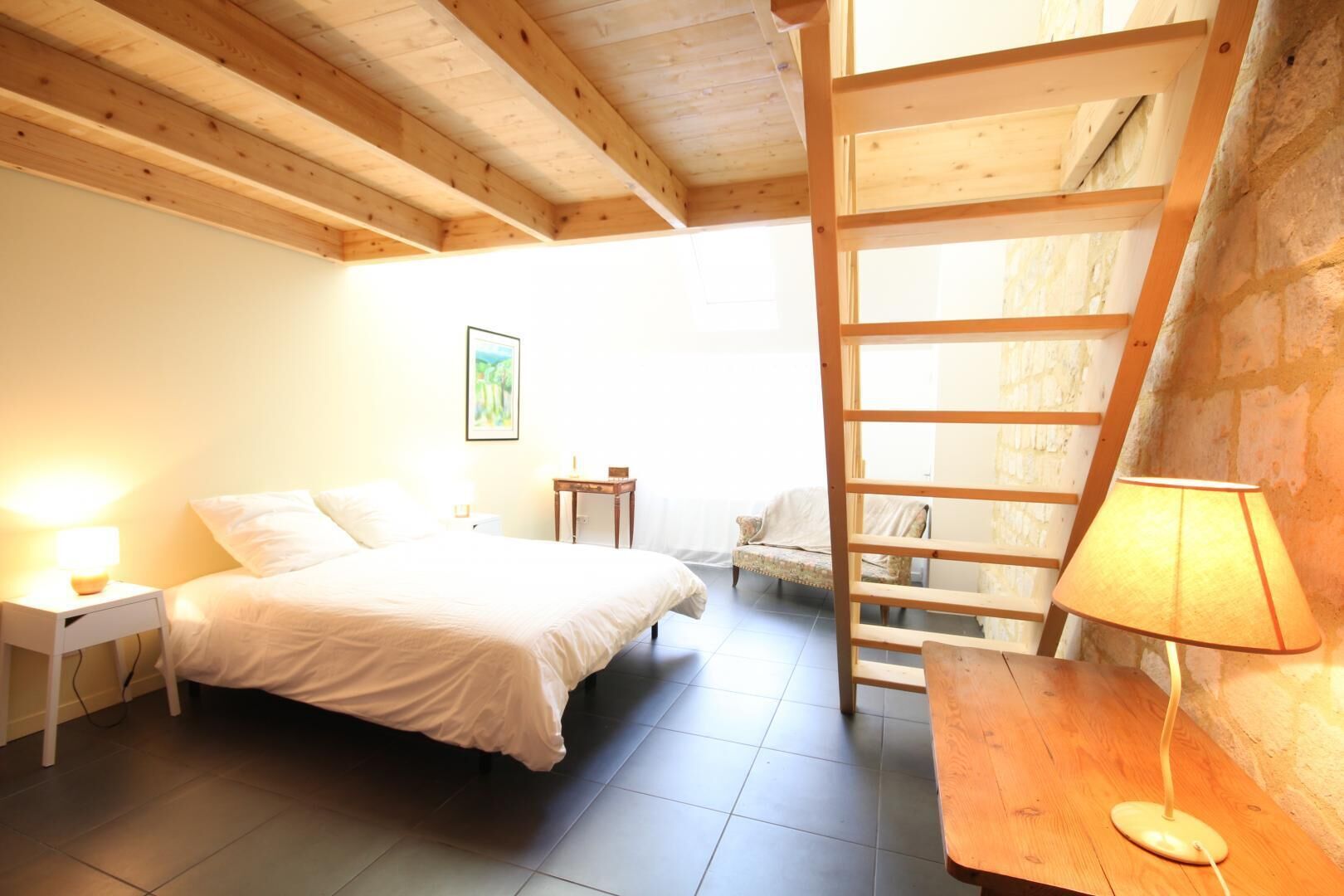 Una camera da letto con un letto, un comodino, una lampada e una scala in legno.