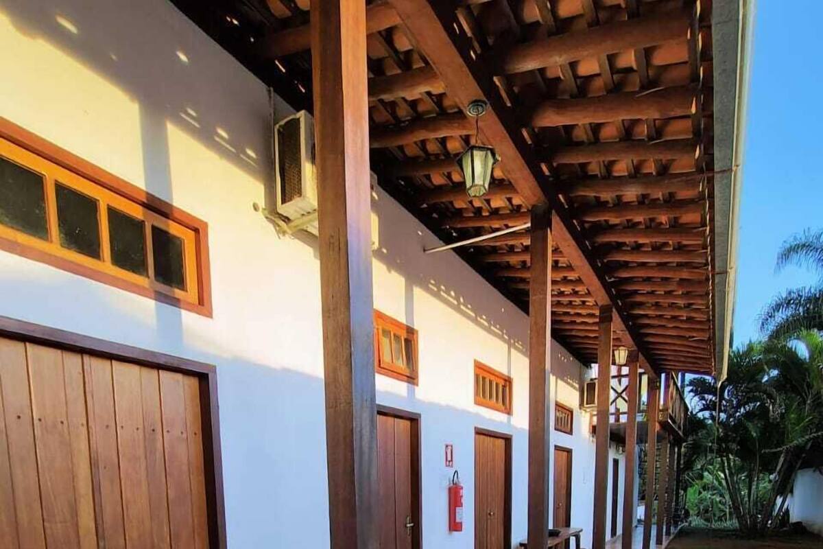 Un espacio al aire libre cubierto con pilares de madera, suelo de baldosas y una hilera de puertas de madera cerradas.