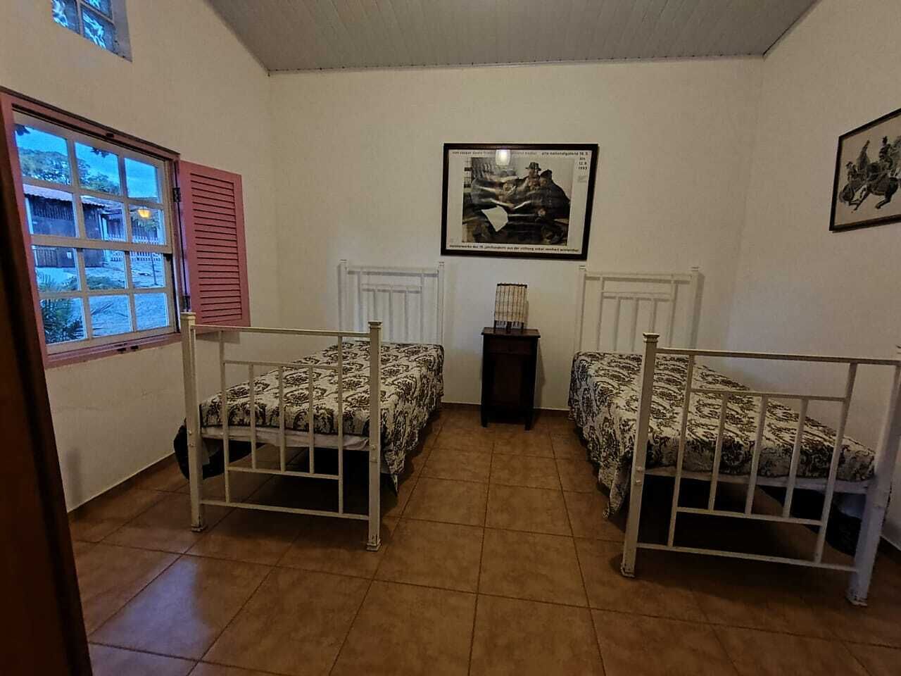 A room with two beds, a window with shutters, a radiator, and a framed picture on the wall.