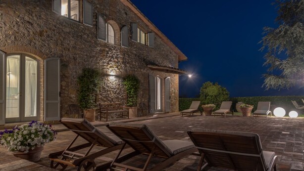 A stone building with a patio area featuring lounge chairs and potted plants. - Villa Porri by MMega (Siena)