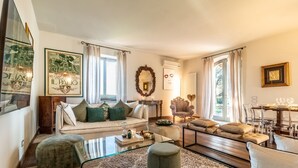 A living room with a sofa, ottoman, armchair, and glass coffee table. - Villa Porri by MMega (Siena)