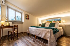Une chambre à coucher avec un lit, un bureau, une chaise, une fenêtre et un tableau accroché au mur.