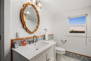 A bathroom with a white sink, wooden vanity, a large mirror, and a window with a view of the sky.