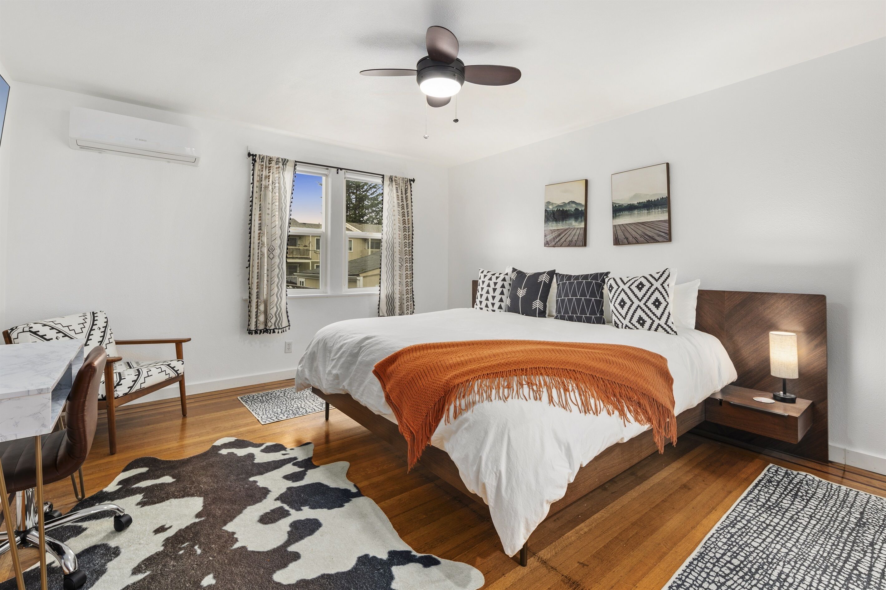 Un dormitorio con cama, escritorio, silla, ventilador de techo y ventana con cortinas.