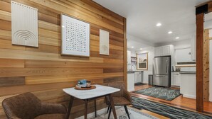 Cocina moderna con paneles de madera, un refrigerador de acero inoxidable y una zona de comedor con dos sillas y una mesa.