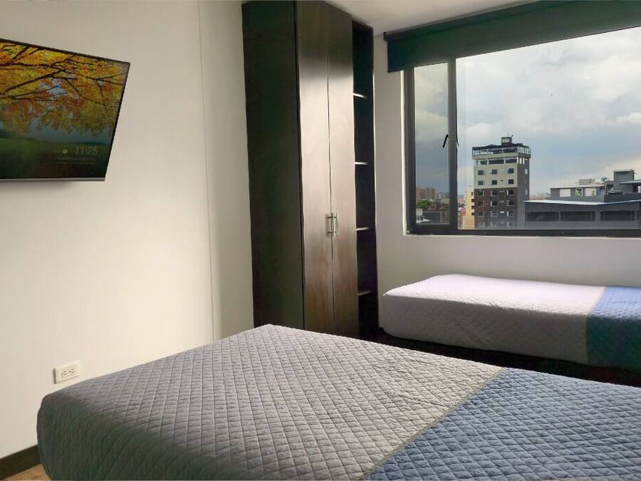 Un dormitorio con cama, ventana con vista a la ciudad, armario y un cuadro en la pared.