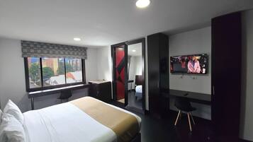 Ein Hotelzimmer mit Bett, Schreibtisch, Stuhl, Fernseher und einem Fenster mit Blick auf die Stadt.